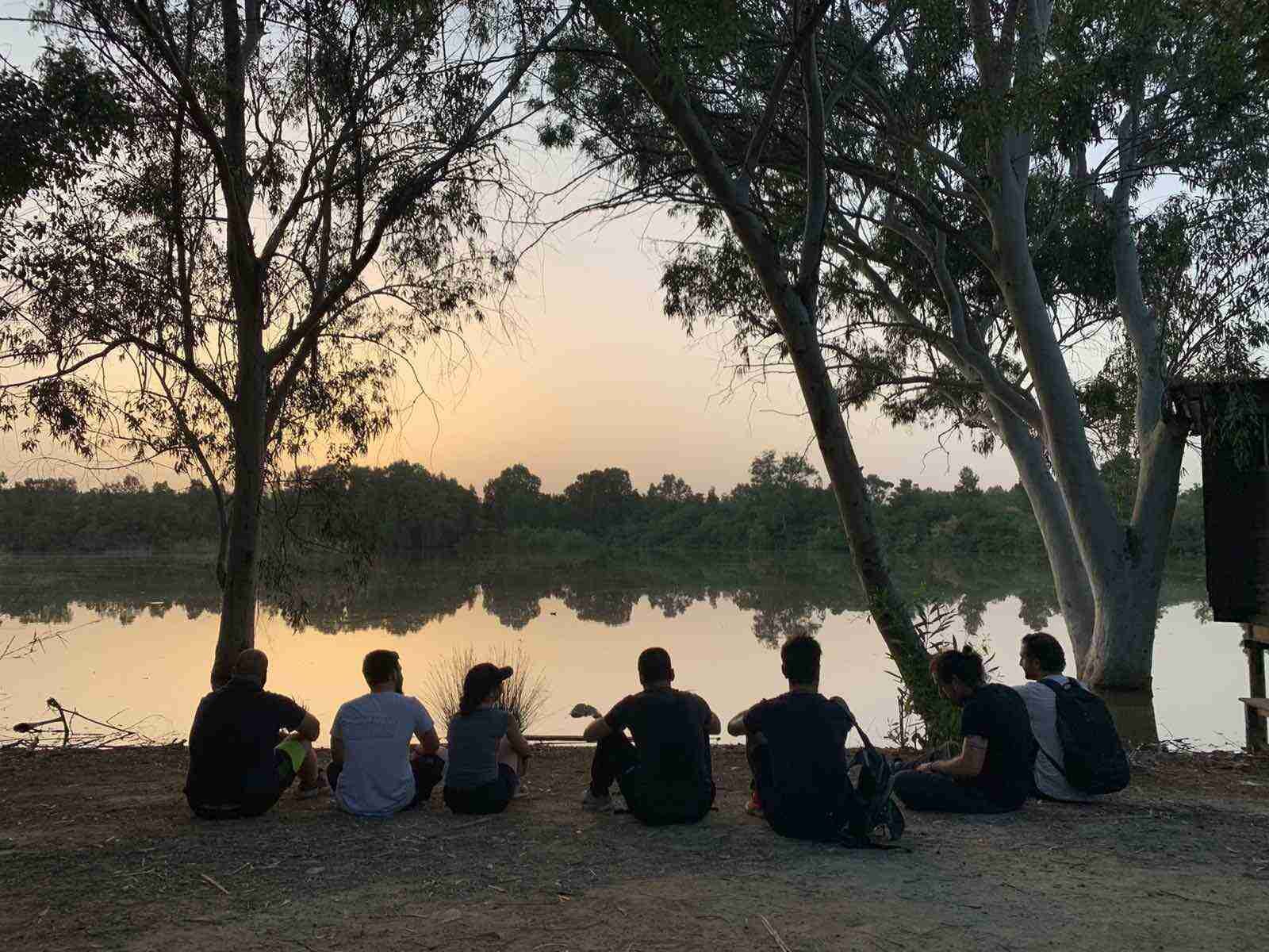 A group Of friends sitting by a lake on sunset time