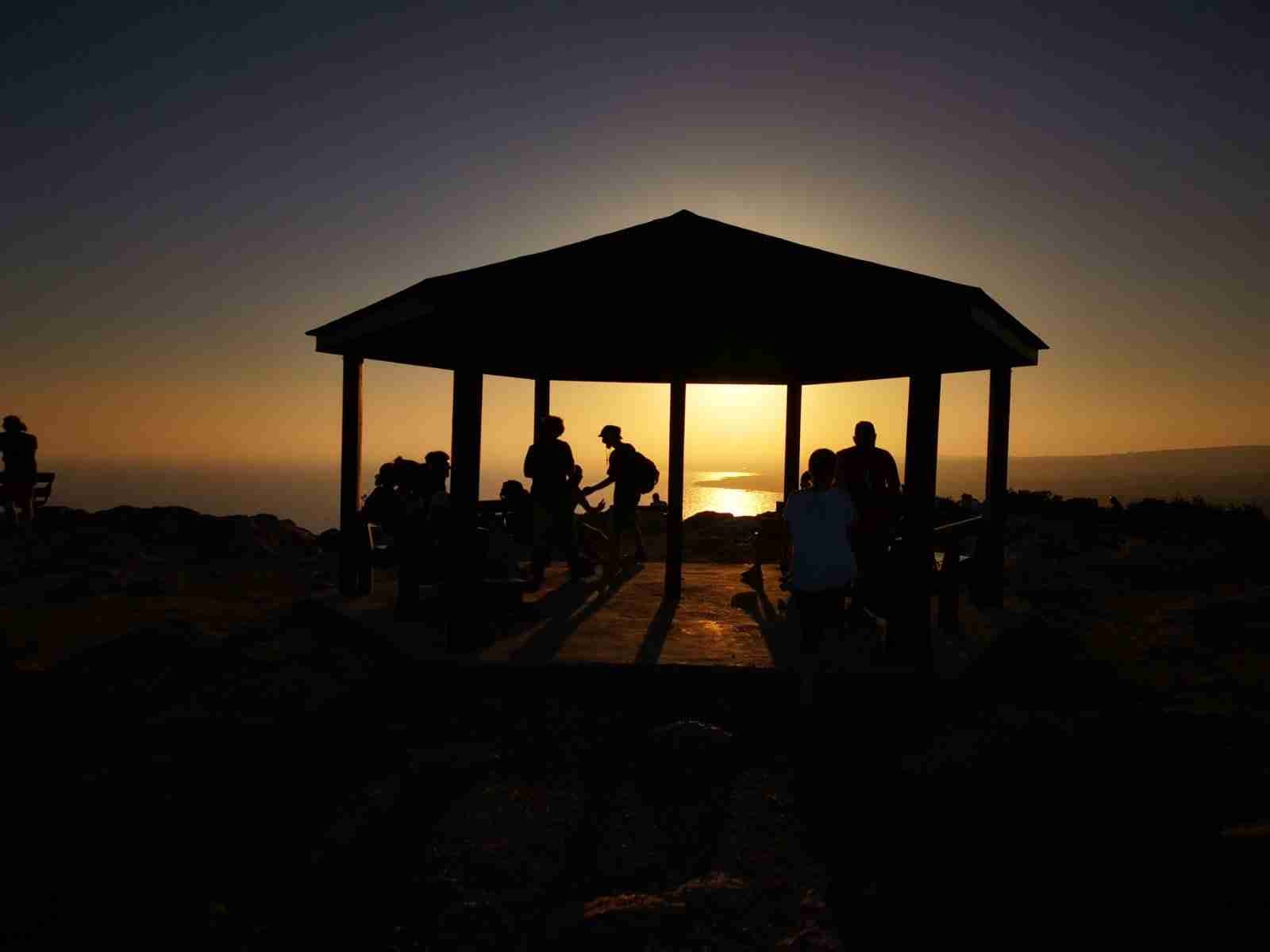 A kiosk with some people sitting by the sunset